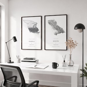May include: Two framed vertical wall art prints featuring detailed grayscale topographic maps of Isabela and Rincón, Puerto Rico. Each print includes the location name in bold black text, followed by Puerto Rico and geographic coordinates.