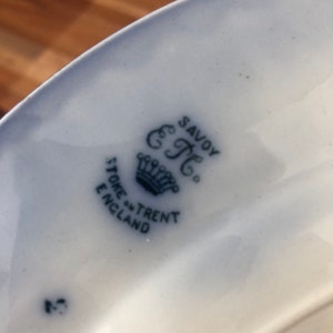 May include: Close-up of a blue and white ceramic plate with a crown and the text "Savoy" "C.T." "Stone-Trent" "England" printed on the bottom.
