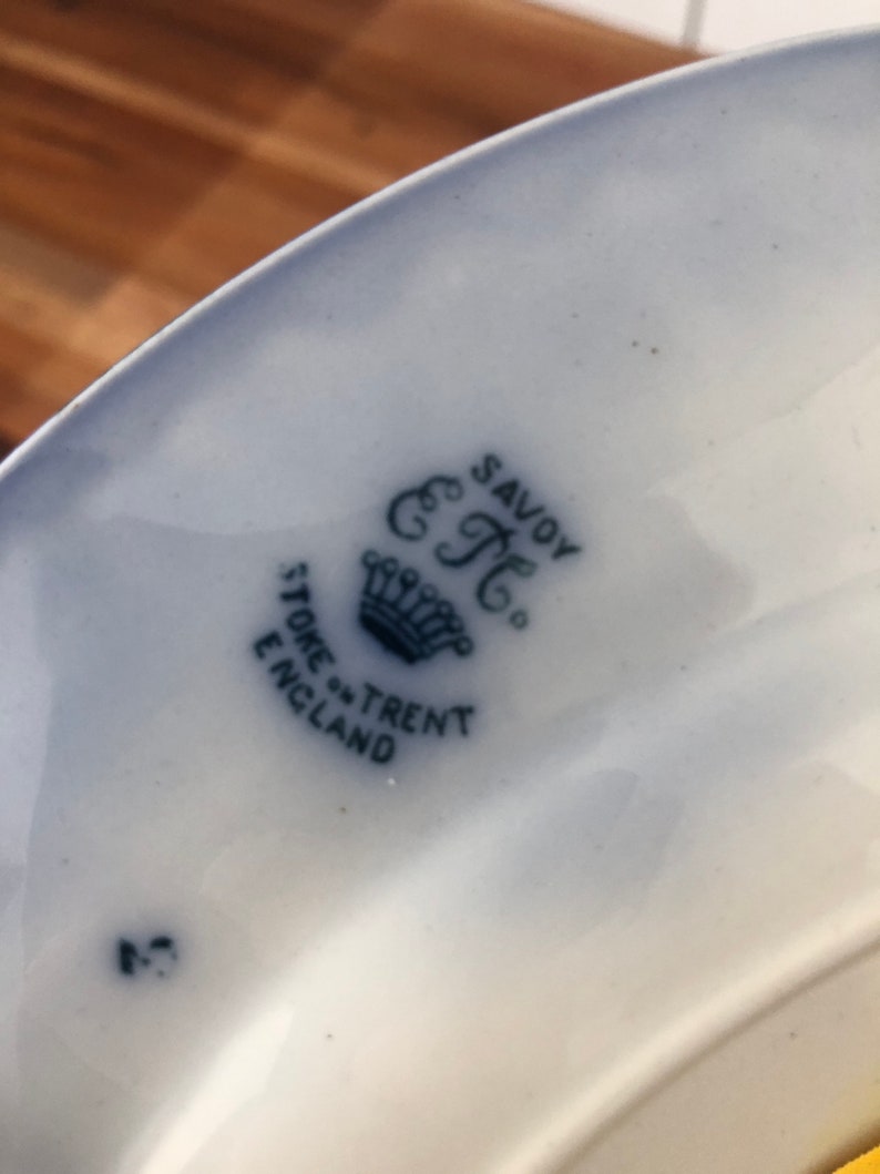 May include: Close-up of a blue and white ceramic plate with a crown and the text "Savoy" "C.T." "Stone-Trent" "England" printed on the bottom.