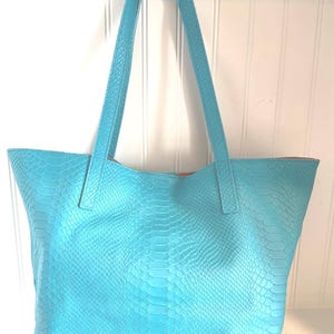 May include: A turquoise tote bag with a snakeskin texture. The bag has two long handles and a spacious interior. The bag is made of a faux leather material and is a bright, eye-catching color.