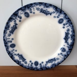 May include: A white ceramic plate with a blue and white floral pattern around the edge. The plate is on a wooden surface.