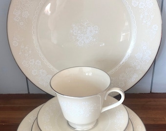 May include: A set of white porcelain dinnerware with a delicate floral pattern and a silver rim. The set includes a dinner plate, a salad plate, a saucer, and a teacup.