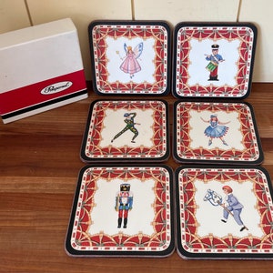 May include: Set of six square coasters with a red, white, and black border. Each coaster features a different illustration of a character from the Nutcracker ballet. The illustrations include a ballerina, a soldier, a nutcracker, a fairy, and a horse and rider. The coasters are made by Pfaltzgraff.