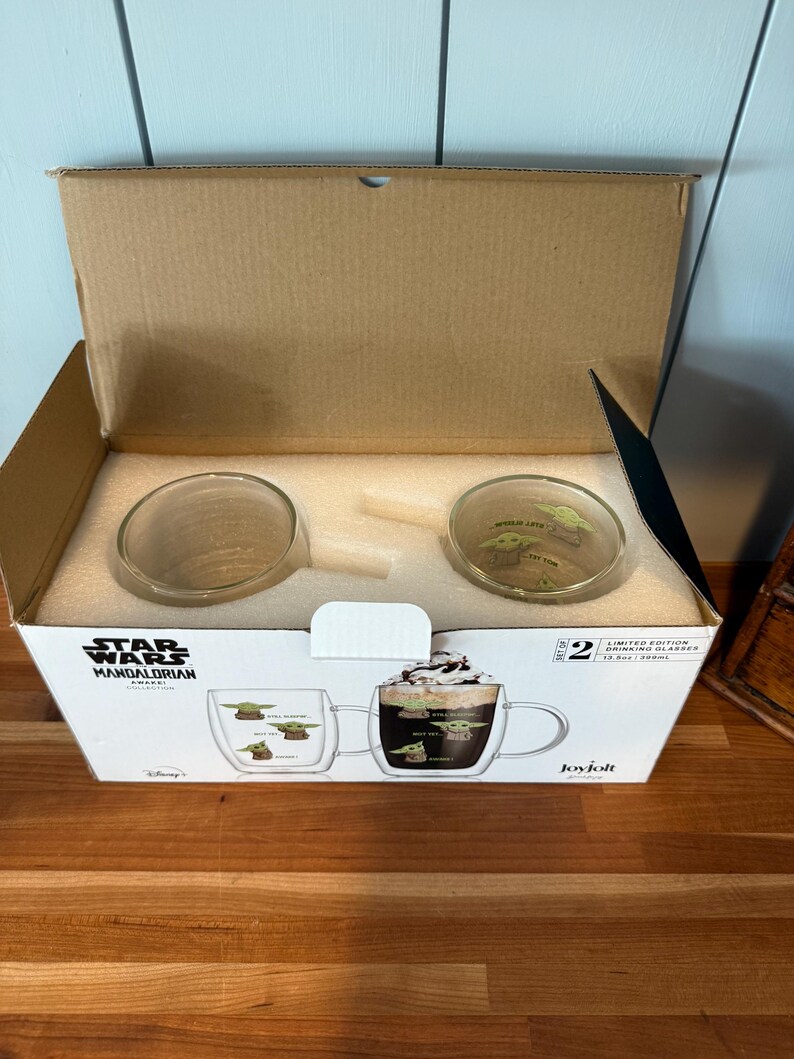 K&ouml;nnte beinhalten: Ein Karton mit zwei transparenten Glasbechern mit Griffen. Die Becher zeigen ein Design von Grogu aus The Mandalorian. Die Box hat das Star Wars Mandalorian Collection Logo und den Text "Limited Edition Drinking Glasses".