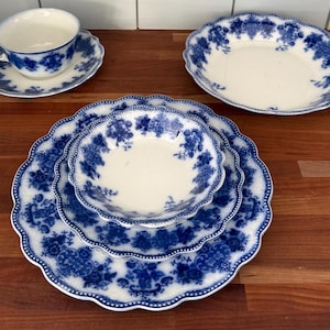 May include: A collection of blue and white porcelain tableware, including a teacup and saucer, an oval serving dish, and several plates and bowls. The pieces feature a floral pattern and scalloped edges, creating a classic and elegant aesthetic.