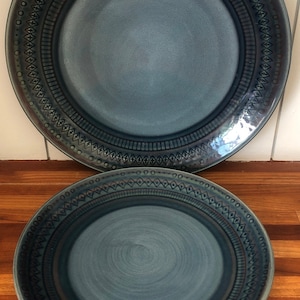 May include: Two blue ceramic plates with a geometric pattern around the rim. The larger plate has a smooth surface, while the smaller plate has a textured surface.