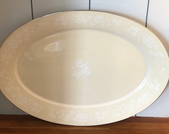 May include: A large, oval-shaped serving platter with a cream-colored background and a delicate white floral pattern around the edge.