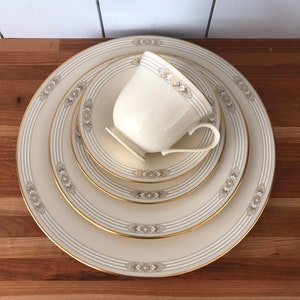 May include: A set of four ivory-colored ceramic plates with gold trim and a delicate floral pattern. The plates are stacked with a matching ivory-colored teacup with gold trim and a floral pattern on top.