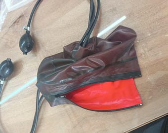 May include: A dark maroon inflatable cuff featuring a bright red interior lining and a black zipper closure. The cuff is connected to two black rubber tubes, each ending in a black hand-operated air pump bulb with a small metal valve at the top.