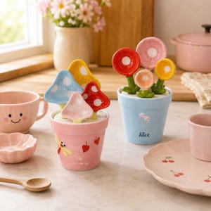 May include: Two ceramic flower pots containing mushroom-shaped measuring spoons. The pink pot features a dragonfly and the name Lily with 2025.06.18. The blue pot features the name Alice. Both pots include colorful, polka-dotted mushroom spoons.