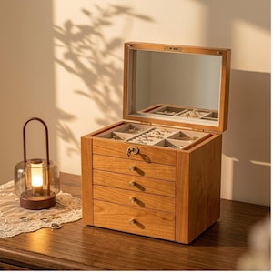 May include: A wooden jewelry box with a hinged lid featuring an interior mirror, four pull-out drawers with small round knobs, and a top compartment with ring slots and open storage sections. The box has a light brown finish and a metal key lock.