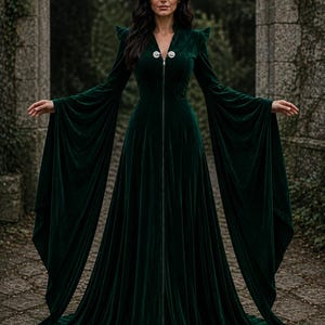 May include: A floor-length dark green velvet gown featuring long, wide bell sleeves, structured shoulders, and a full-length front zipper closure. The garment has a V-neckline and a fitted bodice that flares into a voluminous, flowing skirt.