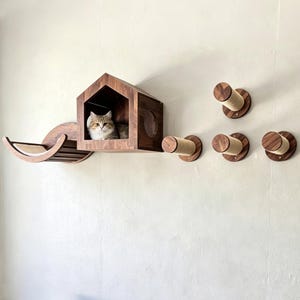 May include: A wall-mounted cat furniture set featuring a dark wood house-shaped enclosure with a cat inside, a curved wooden hammock with a light-colored cushion, and four cylindrical wall-mounted steps wrapped in tan sisal rope.