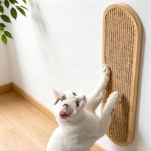 May include: A vertical, oval-shaped wall-mounted cat scratching post featuring a light-colored wooden frame and a textured, woven sisal fiber surface. The scratching post is mounted on a plain white wall, providing a functional surface for scratching.