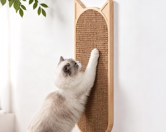 May include: A wall-mounted cat scratching post featuring a light wood frame shaped like cat ears with a textured brown sisal fiber scratching surface. A fluffy white and grey cat is shown reaching up to scratch the vertical panel.