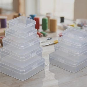 May include: A collection of clear, rectangular plastic storage boxes with hinged lids and snap closures. The boxes are arranged in two separate stacks of varying sizes, featuring a smooth, semi-transparent finish and a simple, functional design.