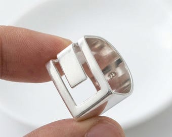 May include: A silver ring featuring an open, geometric square design with a smooth, polished finish. The interior band of the ring is clearly stamped with the number 925, indicating the silver content of this piece of jewelry.