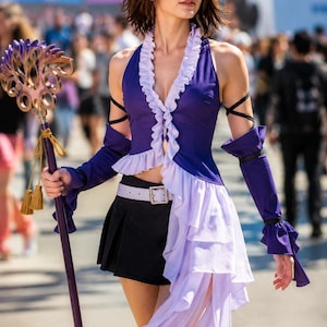 May include: A purple sleeveless top with light purple ruffled trim, a black pleated mini skirt, a light purple belt with a silver buckle, and purple arm sleeves. A long purple staff with a decorative gold-toned top and gold tassels is held.