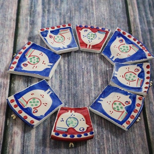 May include: A collection of hand-painted ceramic coasters arranged in a circle. Each coaster features a bird design with blue, red, and white colors. The coasters are on a wooden surface.