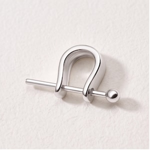 May include: A silver-toned metal shackle-style jewelry component featuring a U-shaped body and a straight pin that slides through the ends. The pin has a small spherical bead at one end, providing a secure closure mechanism for this piece.