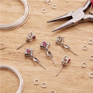 Puede incluir: Enganches para joyería en tono plateado con una pequeña piedra preciosa redonda de color rosa engastada en un diseño recortado en forma de corazón. Estos componentes metálicos incluyen un perno vertical para cuentas, bobinas de alambre y anillas.