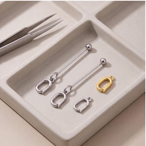 Puede incluir: Dos componentes de joyería de metal plateado estilo barra con cierres de resorte ovalados adjuntos, un cierre de resorte ovalado plateado adicional y un cierre de resorte ovalado dorado, todo dispuesto con un par de pinzas de metal.