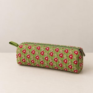 May include: A cylindrical pencil case featuring a quilted green fabric exterior with a repeating pattern of small red flowers and green stems. The case includes a green zip closure along the top and a small fabric loop on the left side.