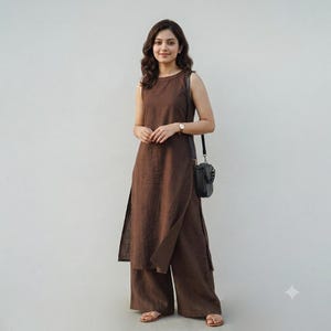 May include: A sleeveless dark brown tunic with a high neckline and side slits, paired with matching wide-leg trousers. The outfit is accessorized with a small black crossbody bag featuring a chain strap and simple brown flat sandals.