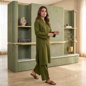 May include: An olive green long-sleeved tunic with a button-down placket and matching wide-leg trousers. The tunic features a V-neckline and side slits, paired with brown slide sandals. The outfit is a solid, monochromatic set in a plain fabric.