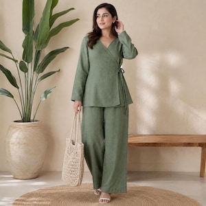 Puede incluir: Un conjunto de dos piezas en color verde salvia que consta de una blusa cruzada de manga larga con cierre de lazo lateral y pantalones a juego de pierna ancha. El conjunto se completa con un bolso tote tejido en color crema con diseño calado.