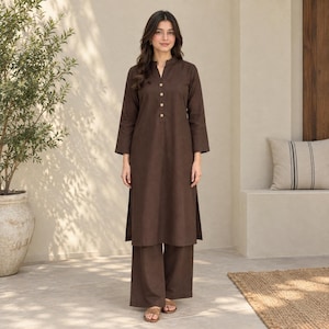May include: A dark brown long-sleeved tunic featuring a mandarin collar and a partial button-down front with four metallic buttons, paired with matching wide-leg trousers. The ensemble is crafted from a solid-coloured fabric with a smooth texture.
