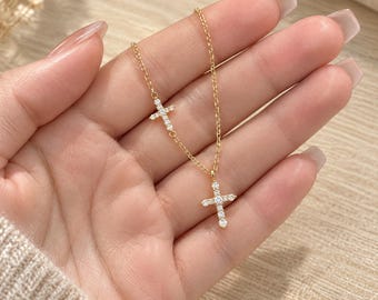 Puede incluir: Un collar de cadena dorada con dos pequeños colgantes de cruz, cada uno incrustado con piedras transparentes y brillantes. El collar tiene un diseño de cadena de eslabones finos, con una cruz situada en la cadena y la otra como colgante.