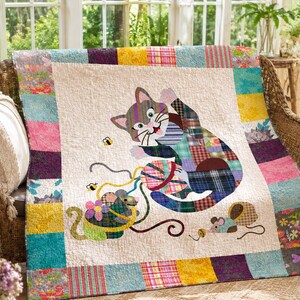 Pode incluir: Uma colcha de retalhos com um painel central creme apresentando a aplicação de um gato cinzento a brincar com um novelo de lã multicolorido, um pequeno rato e duas abelhas. A colcha é emoldurada por uma borda de quadrados de tecido coloridos.