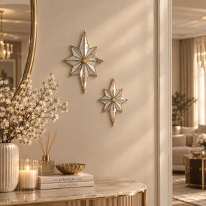 May include: Two star-shaped wall mirrors with gold-toned metal frames and faceted glass panels. The larger mirror is positioned above the smaller one, both featuring a multi-pointed design that reflects light across the wall surface.