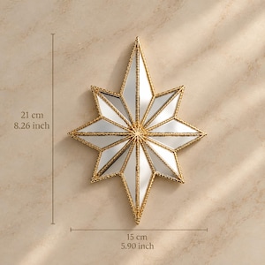 May include: A star-shaped wall mirror with a gold-toned textured frame. The mirror features eight pointed rays and measures 8.26 inches in height by 5.90 inches in width. The reflective surface is divided into triangular segments by the gold frame.