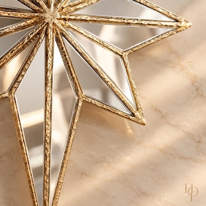 May include: A multi-pointed star-shaped decorative object featuring a textured gold metal frame and mirrored glass panels. The design consists of sharp, elongated points radiating from a central point, creating a geometric star silhouette.