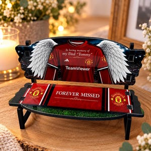 May include: A decorative miniature bench featuring a red Manchester United football shirt graphic with white angel wings, the text In loving memory of my Dad Tommy, and the text FOREVER MISSED on the seat, accented with team logos.