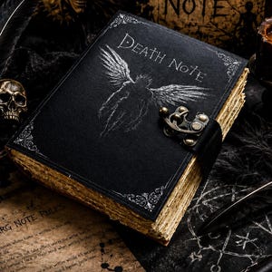 May include: A black hardcover journal titled Death Note with a white winged figure illustration on the cover. The book features a metal latch closure and aged, deckled-edge pages. It is accompanied by a quill pen, a small skull, and a parchment paper.