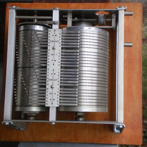 May include: A vintage metal timer with two rotating dials. The dials are labeled with numbers 1 through 12, AM, PM, and Circuit No. 1 and Circuit No. 2. The timer has a silver finish and is mounted on a wooden base.