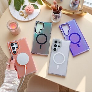 May include: Four rectangular smartphone cases with camera cutouts and integrated magnetic charging rings. One case is orange with a white charger attached, one is iridescent green, one is translucent white, and one is a vibrant purple gradient.