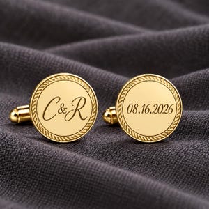 Puede incluir: Un par de gemelos redondos de tono dorado con un borde de textura de cuerda. Un gemelo está grabado con las letras C & R en fuente cursiva, y el otro está grabado con la fecha 08.16.2026 en una tipografía serif clara y legible.
