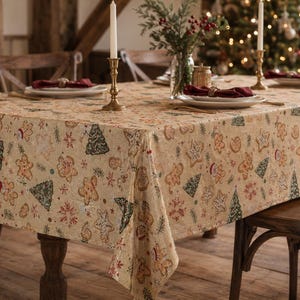 May include: A rectangular tablecloth featuring a repeating pattern of gingerbread people, green Christmas trees, and white snowflakes on a light beige background. The fabric covers a wooden dining table set with plates, napkins, and candles.