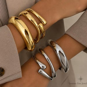 May include: A set of gold-toned and silver-toned metal bangles and cuffs. The gold-toned set includes a thick polished bangle and a thinner open-ended cuff. The silver-toned set features a thick polished bangle and a thinner open-ended cuff.