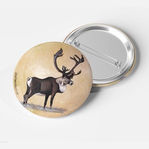 Könnte beinhalten: Ein runder Ansteckbutton mit einer detaillierten Illustration eines Rentiers mit großem Geweih. Das Rentier ist braun und weiß vor einem beigen Hintergrund dargestellt. Der Button hat eine silberne Nadel auf der Rückseite und der Text "jpartwork.co.uk" ist aufgedruckt.