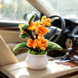 Può includere: Una pianta decorativa realizzata con fiori e foglie di scovolino arancioni e verdi, disposta in un piccolo vaso di ceramica bianca liscia. La pianta presenta molteplici fiori arancioni brillanti con centri bianchi e fogliame verde testurizzato.