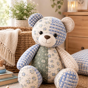 K&ouml;nnte beinhalten: Ein Stoffteddyb&auml;r aus verschiedenen Stoffst&uuml;cken mit blau-wei&szlig;em Vichy-Karo, salbeigr&uuml;nen Blumenmustern und hellbeigen Punkten. Der B&auml;r hat zwei schwarze Knopfaugen sowie eine braun gestickte Nase und einen Mund.
