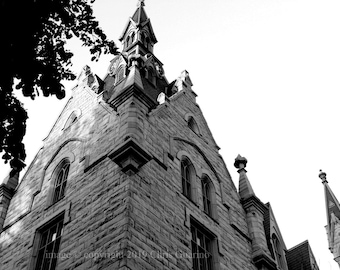 May include: Black and white photograph of a tall, stone building with a pointed roof and multiple windows. The building appears to be a church or cathedral.