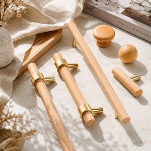 May include: A collection of light-colored wooden cabinet hardware including two long cylindrical pulls with gold metal accents, one shorter cylindrical pull with gold metal accents, one round wooden knob, and one spherical wooden ball.