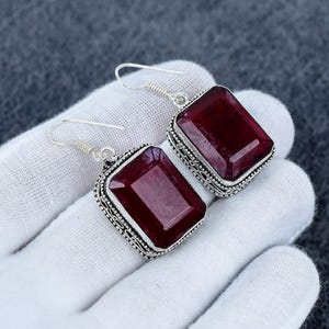 Puede incluir: Un par de pendientes colgantes con grandes piedras preciosas rectangulares de color rojo oscuro facetado, engastadas en monturas de plata esterlina ornamentadas con detalles de cuentas y ganchos de plata simples.