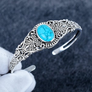 May include: An open cuff bracelet crafted from oxidised silver-tone metal featuring intricate filigree scrollwork and floral patterns. A single oval-shaped turquoise stone with dark veining is set prominently in the centre of the metal band.